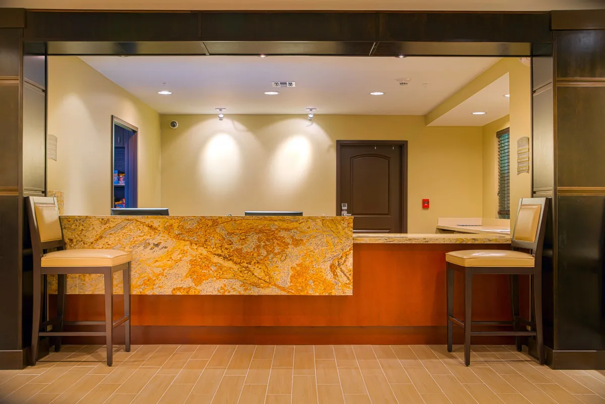 A sleek, modern reception area with a granite desk, comfortable contemporary chairs, and warm wall colors that create an inviting first impression. The space exudes professional hospitality and attentive guest service.