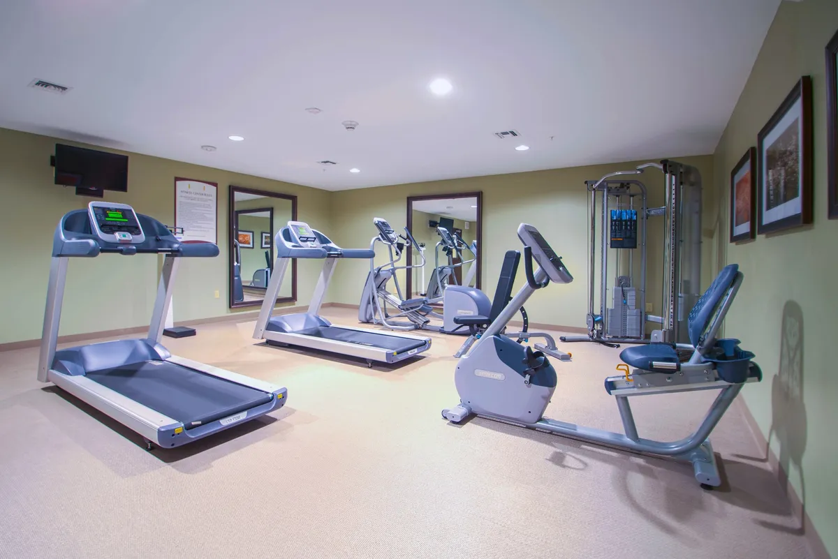 A modern, well-equipped fitness center featuring treadmills, elliptical machines, strength training equipment, and expansive mirrors. The space exudes a motivational atmosphere, with guests engaged in both solo and group workouts, underscoring a sense of community and personal achievement.