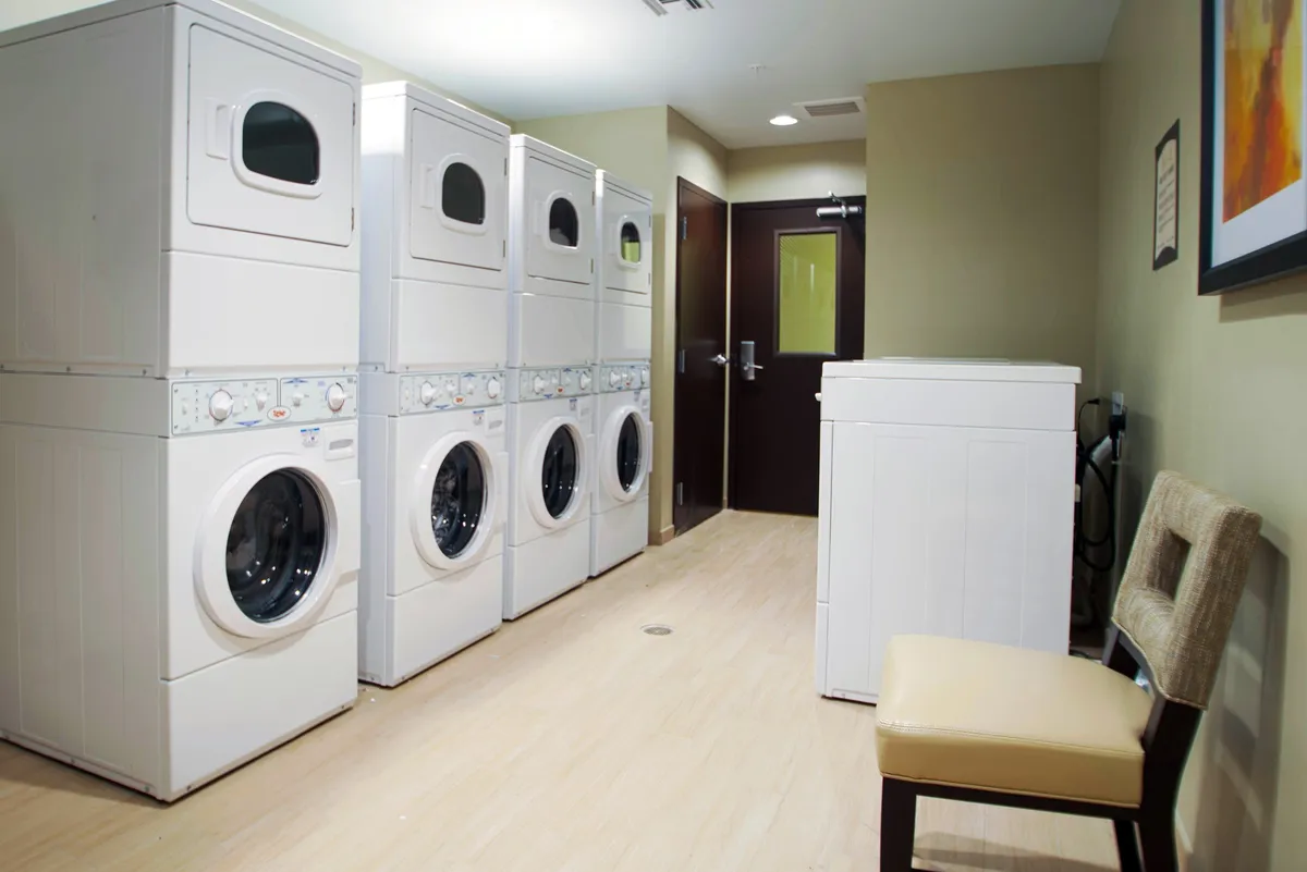 A practical and inviting laundry area showcasing stackable washer and dryer units, a single washing machine, and a cozy seating area. The space is well-organized and clean, suggesting ease and convenience for guests needing to do laundry during longer stays.
