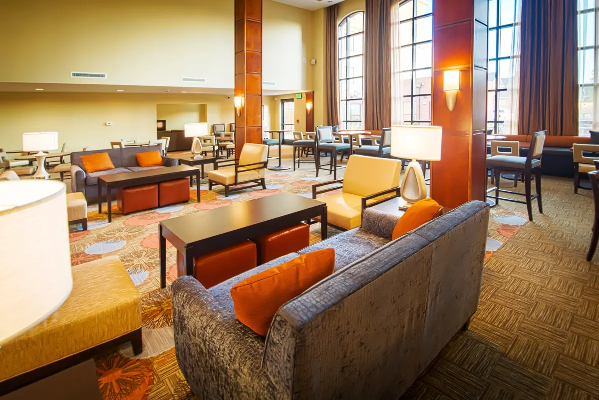 A welcoming studio interior featuring large windows that flood the room with natural light, comfortable seating including a plush sofa, decorative lighting, and vibrant, colorful rugs. The setup encourages relaxation, conversation, and productivity, reflecting an inviting, home-like atmosphere.